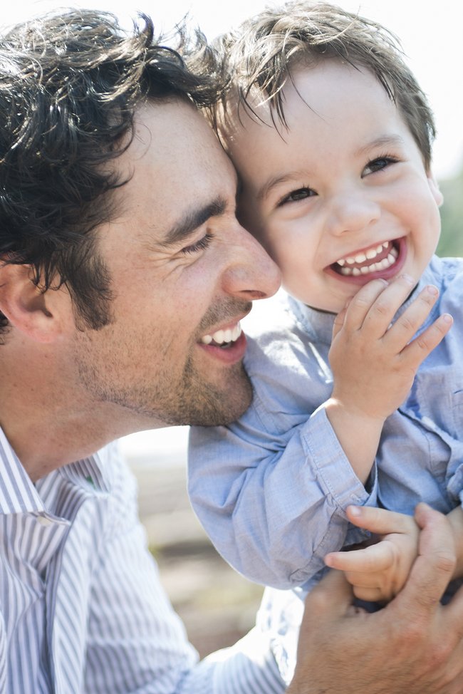 Vater hält seinen Babysohn draußen im Arm und lächelt.